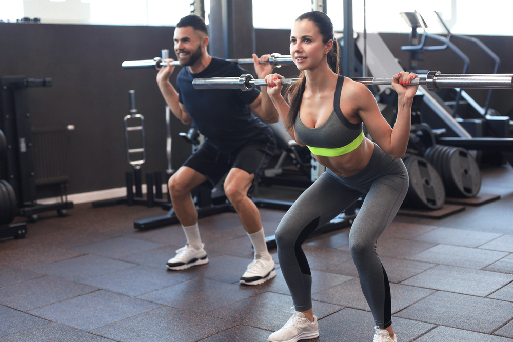 man and woman squatting with barbells