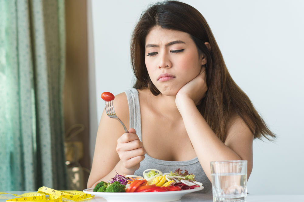 woman staring at a tomato on her fork looking sad