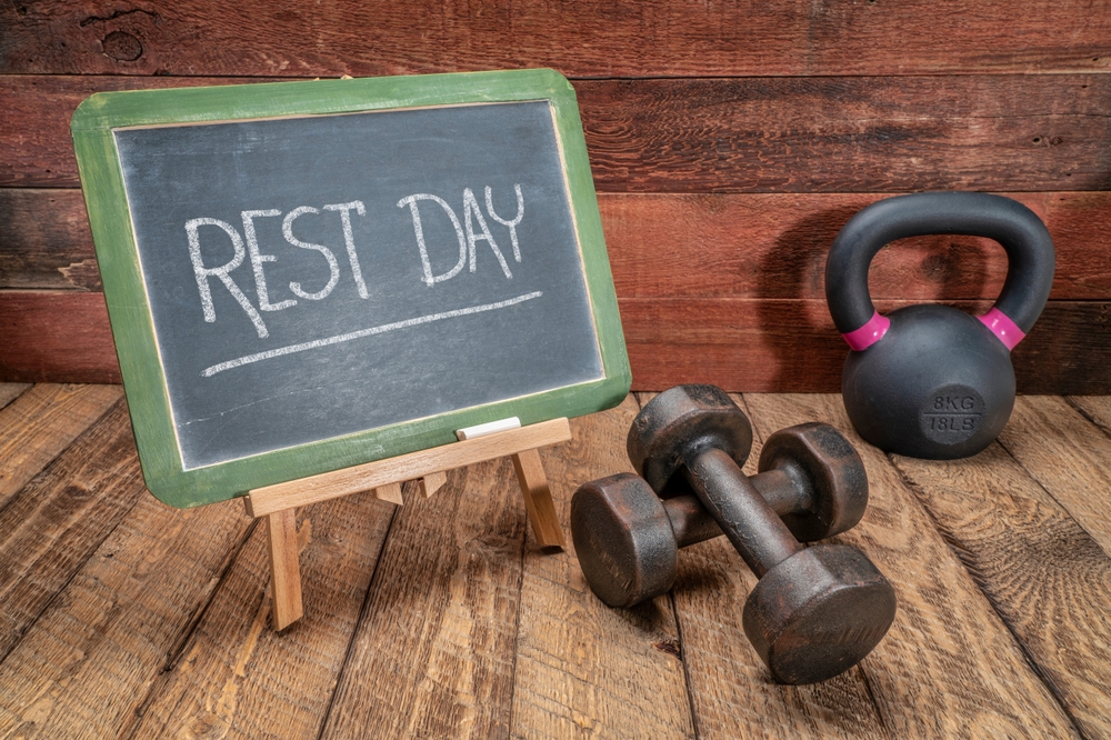 rest day written on chalkboard next to a pair of dumbbells and one kettlebell 